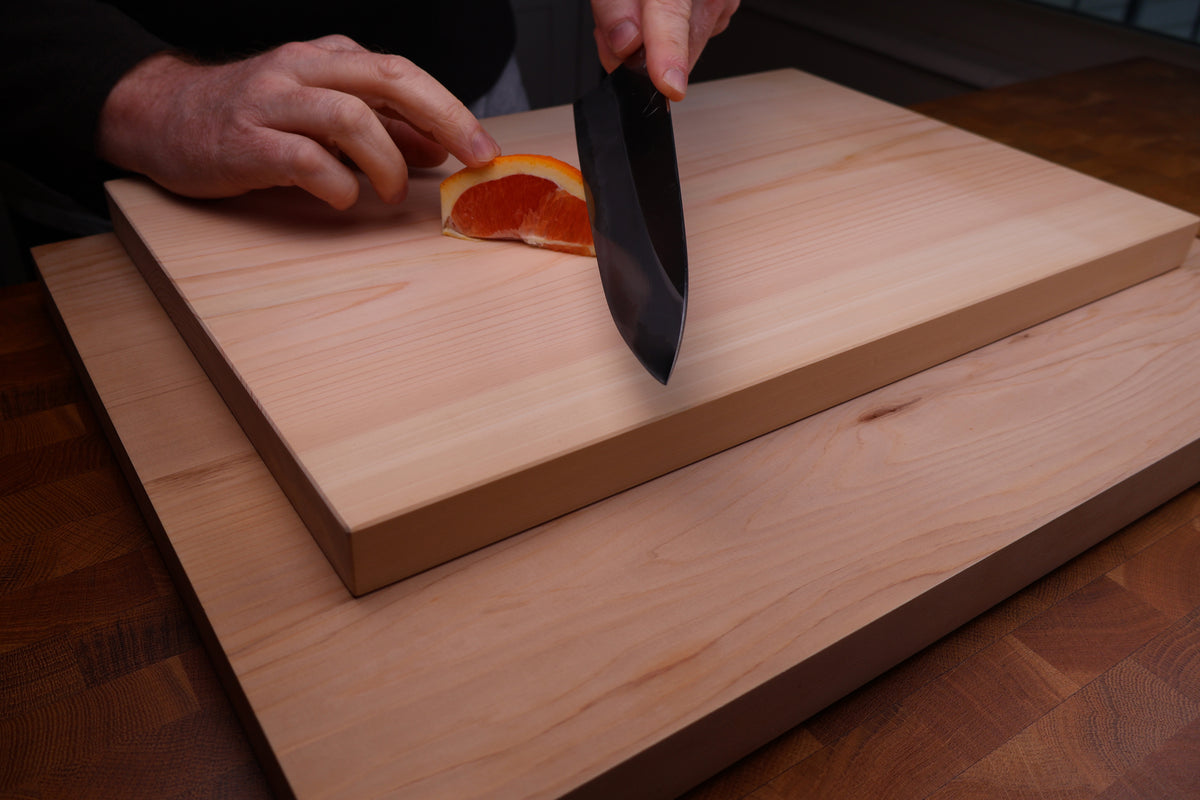 person slicing deep orange colored citrus fruit atop two cream tanned wood cutting boards in dark backdrop