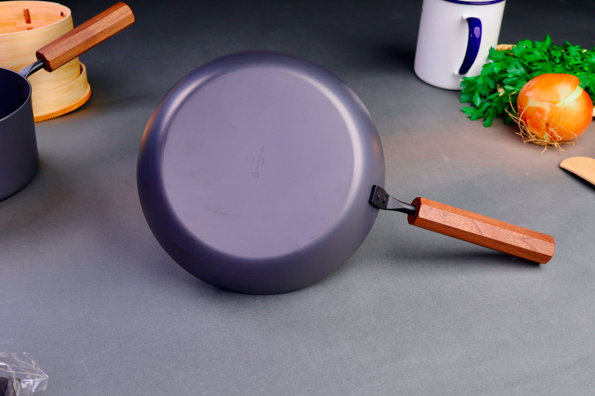 underside of japanese nitrided iron pan surrounded by Japanese kitchenware with light grey background