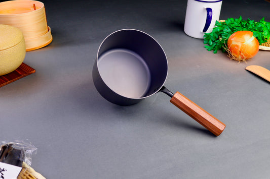 frontal shot of inside round tall black iron saucepan with octagonal wood handle surrounded by japanese kitchenware 