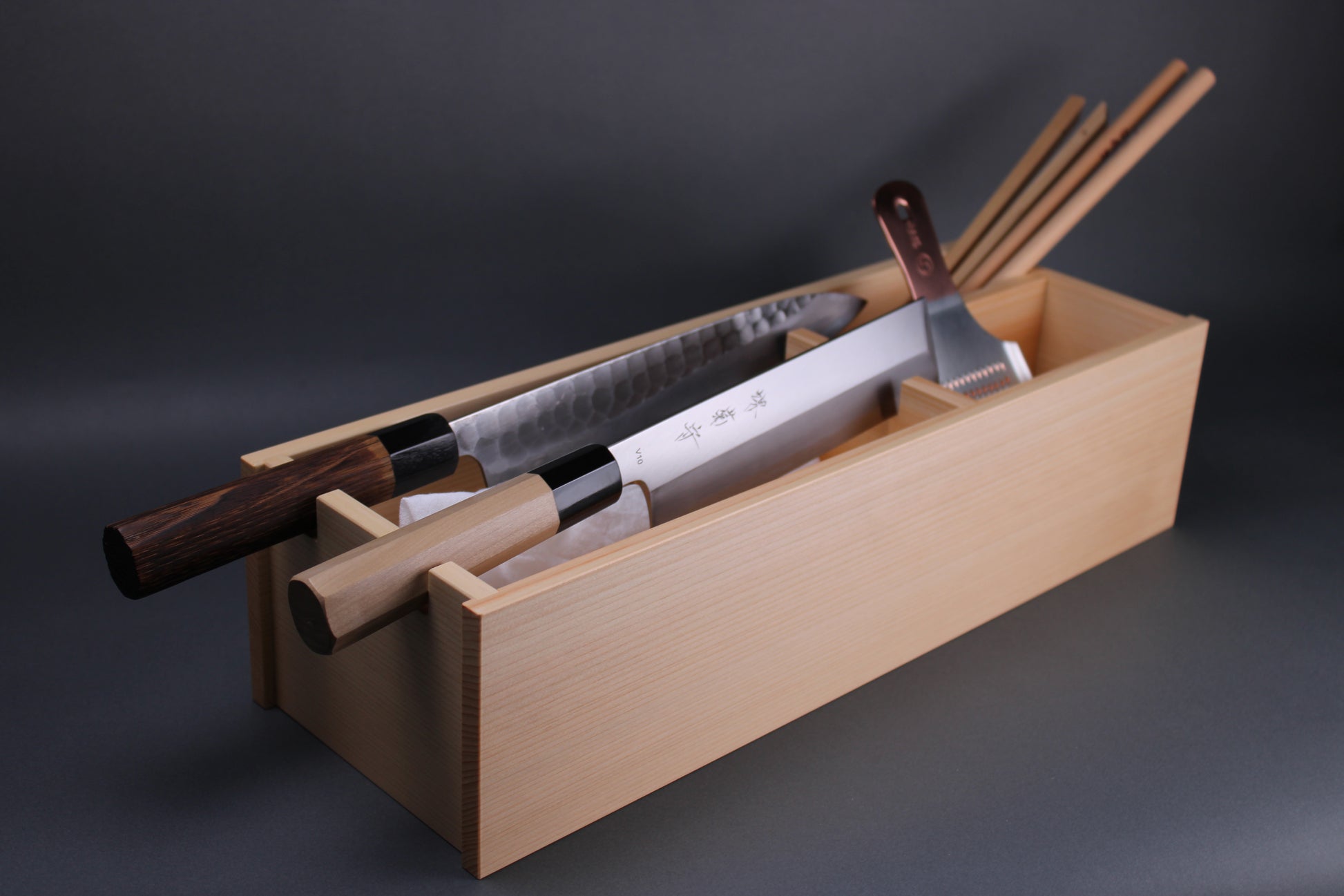 image showing hinoki wood chef toolbox holding two japanese knives copper grater and cooking chopsticks the angled shot displays long dimension of this fine kitchenware that is handmade