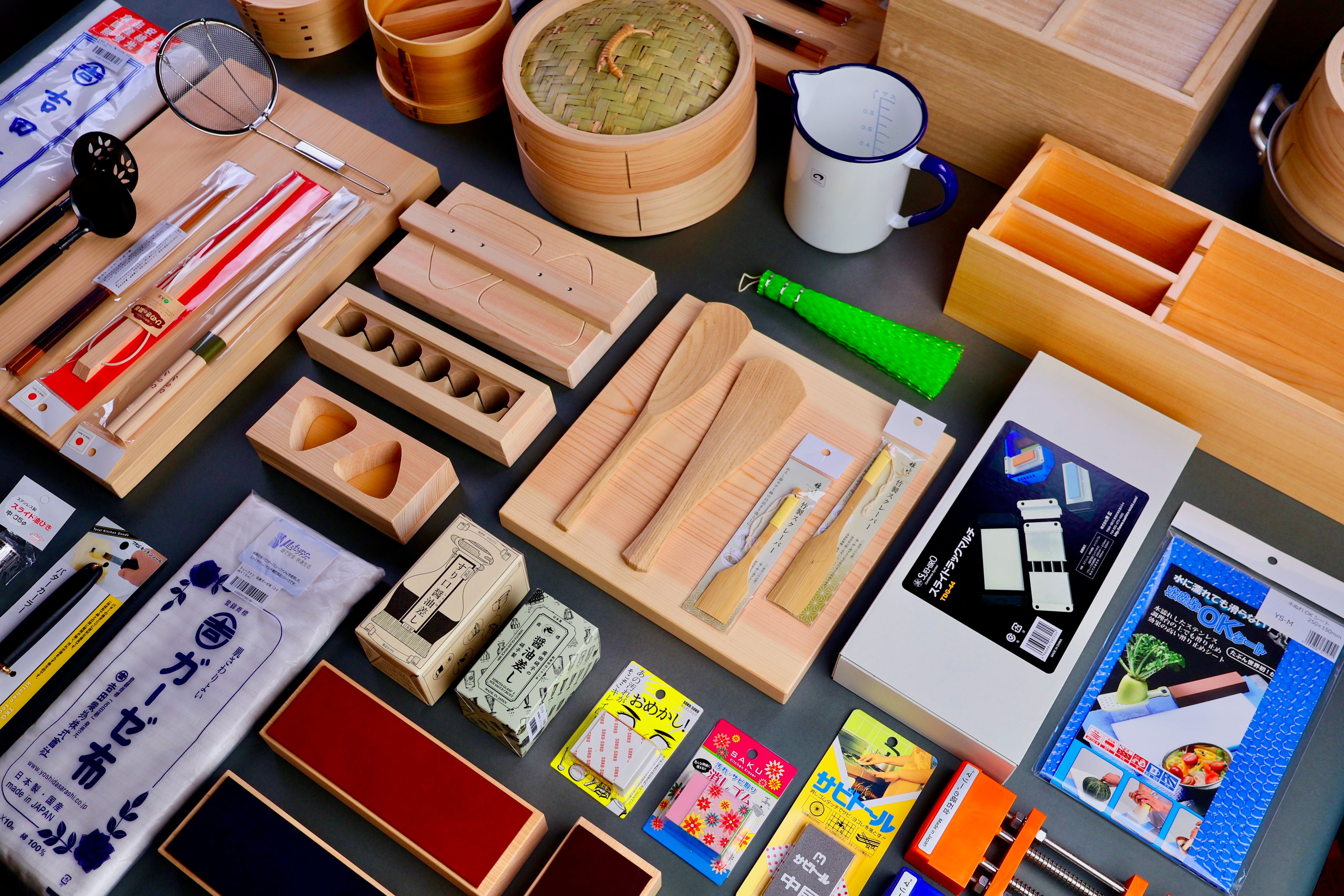 large selection of kitchenware from Japan natal wood board onigiri spoons glass soy sauce cruets in neatly designed boxes on grey background