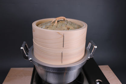 chinese steamer artisan handmade in japan extra thick body sits atop aluminum steam ring and dantsuki seiro steam pot made of aluminum atop a portable gas stove and hinoki cutting board and a grey walled background