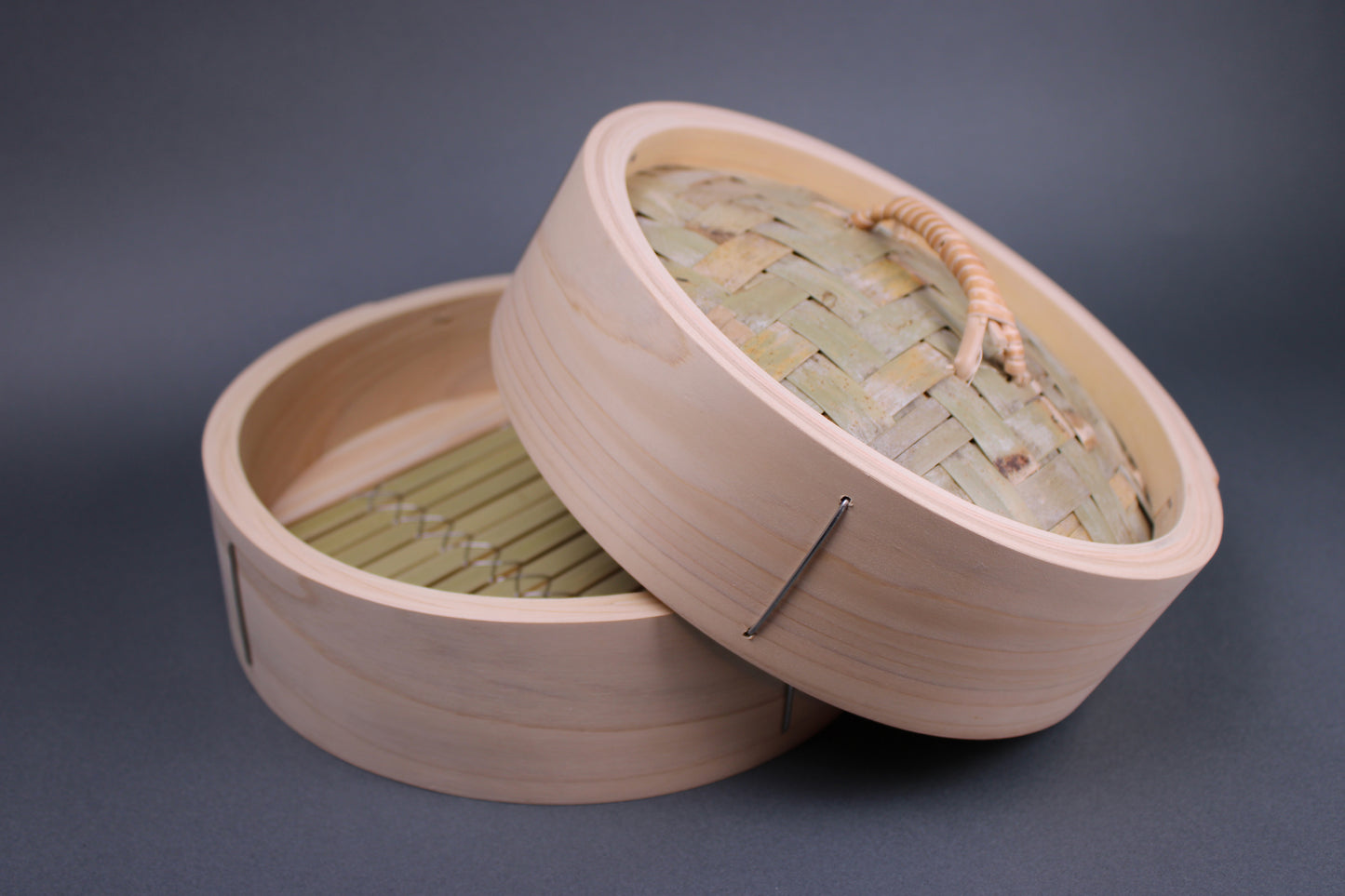  thick kiso hinoki wood base and lid bamboo weaving and rattan woven handle sits askew chinese steamer with thick walls in grey backdrop 