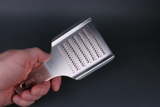 profile shot of hand holding oroshigane copper grater silver shiny body gold colored handle 