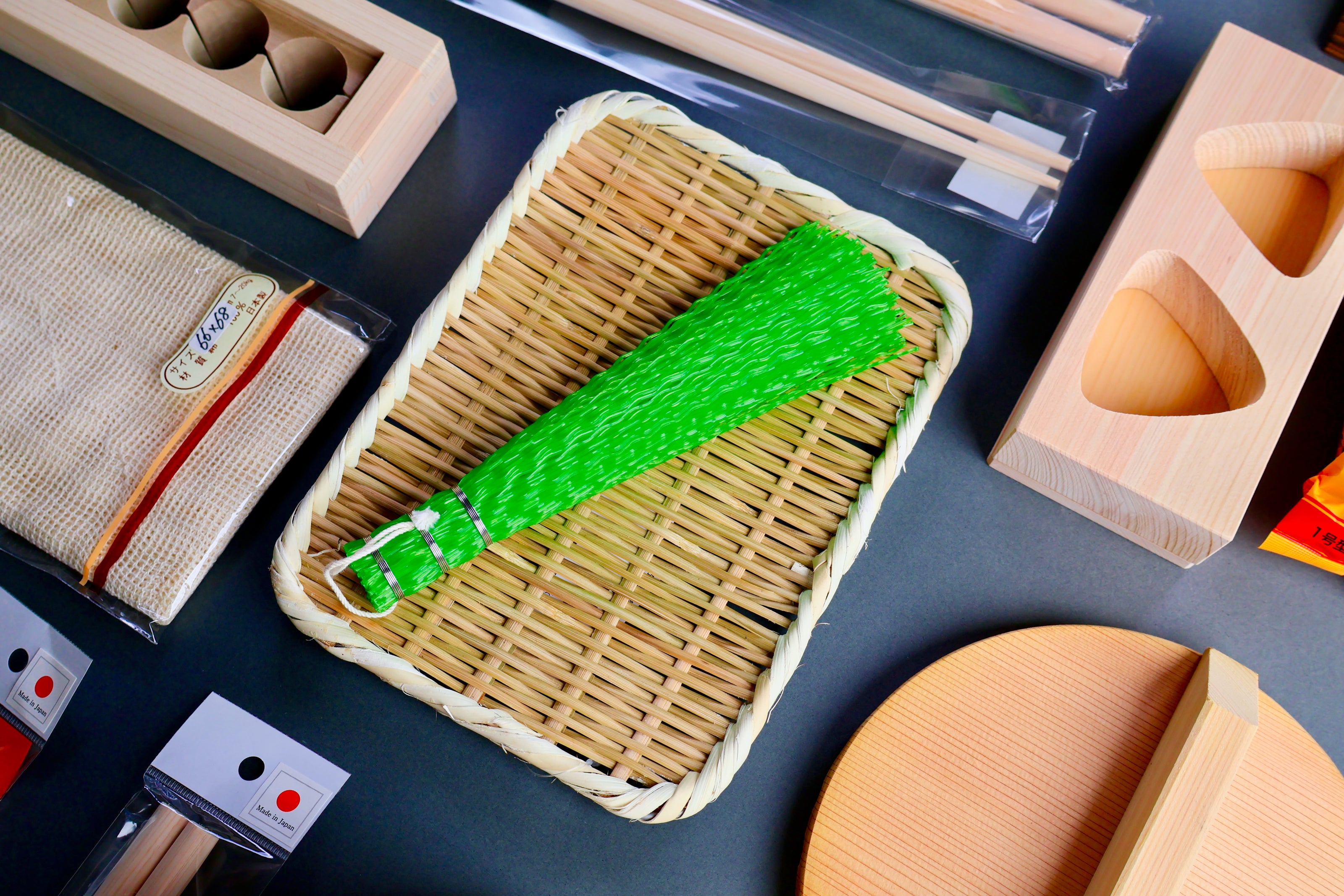 bright green plastic brush atop bamboo woven plate surrounded by japanese kitchenware wood natural products on grey surface