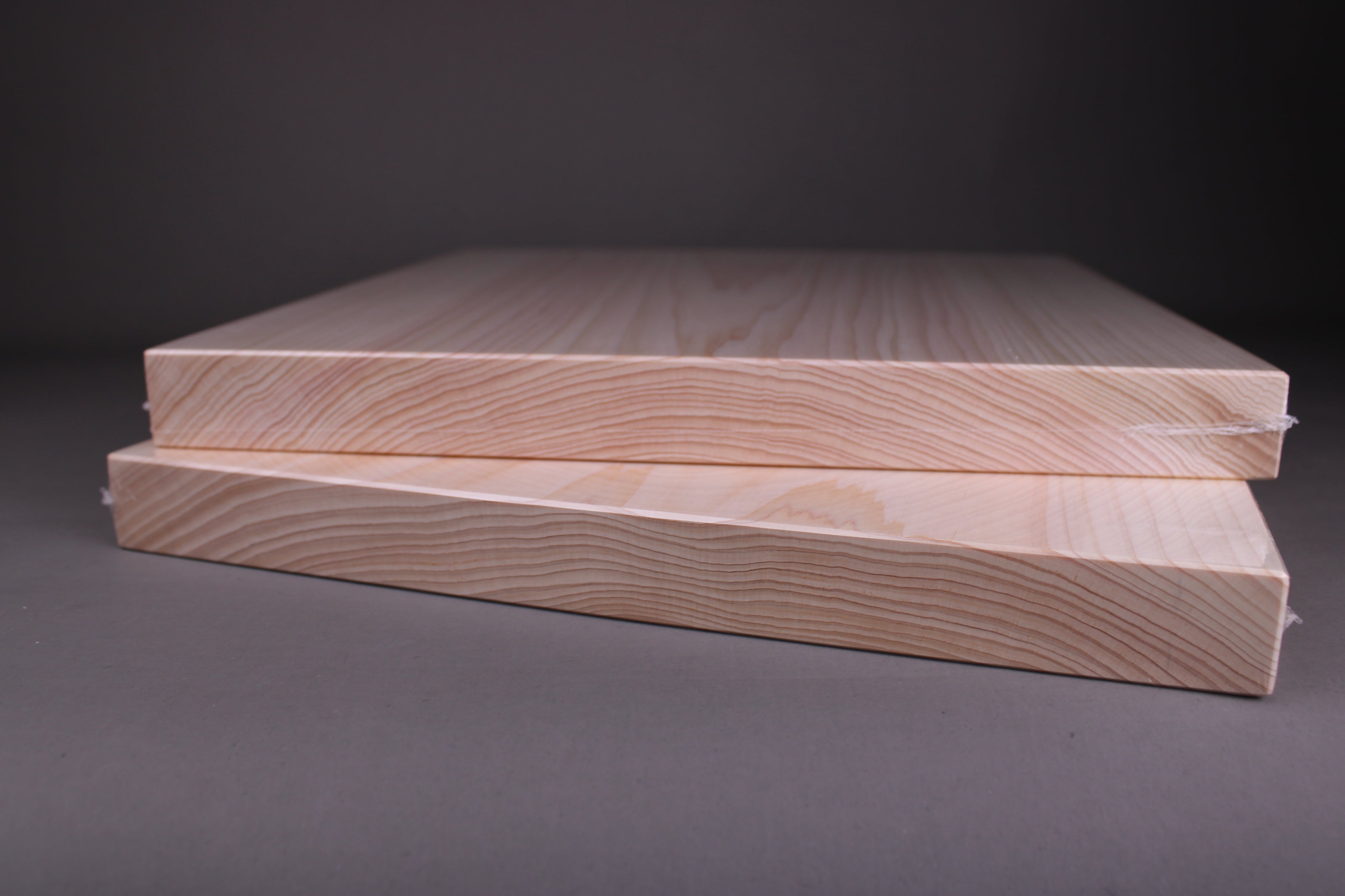 close up profile of two stacked hinoki wood cutting boards showing rings from the grain of wood which is a single piece each the surface is creamy whitish color and very smooth with a grey backdrop