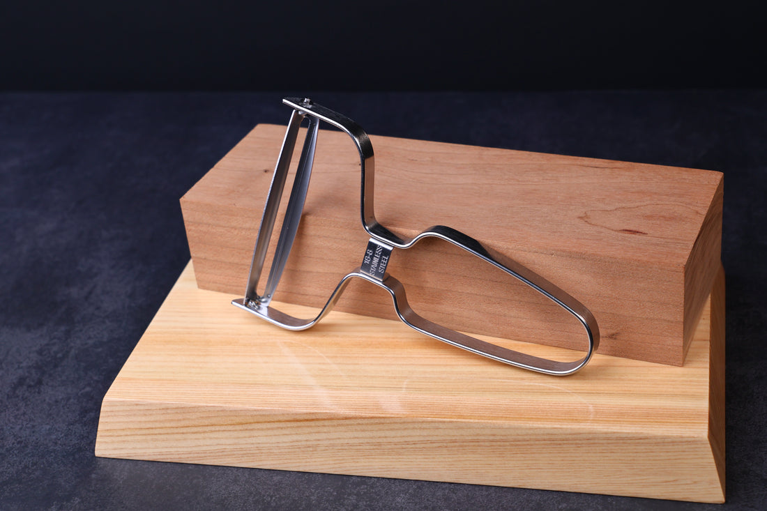 Japanese vegetable peeler large — blade side propped on hinoki blocks showing full peeler profile