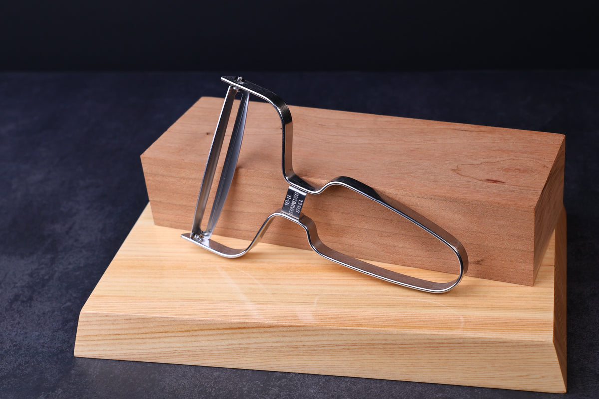 Japanese vegetable peeler large — blade side propped on hinoki blocks showing full peeler profile
