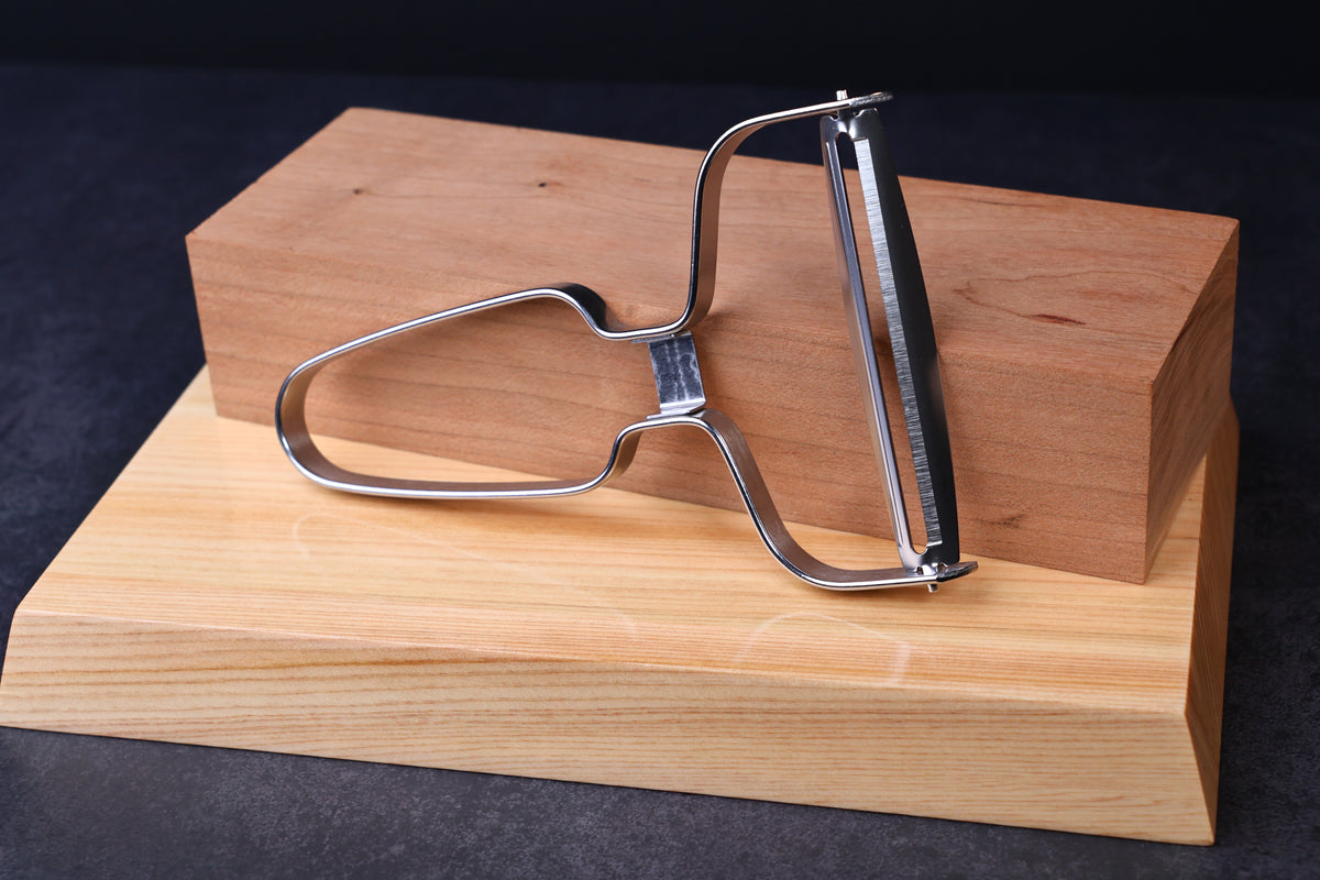 Japanese vegetable peeler large — handle side propped on hinoki blocks showing serrated blade edge detail