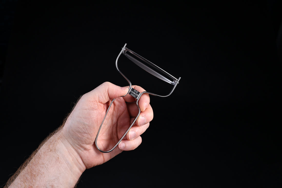 Japanese vegetable peeler large — held in hand, front view showing wide blade and wire frame handle