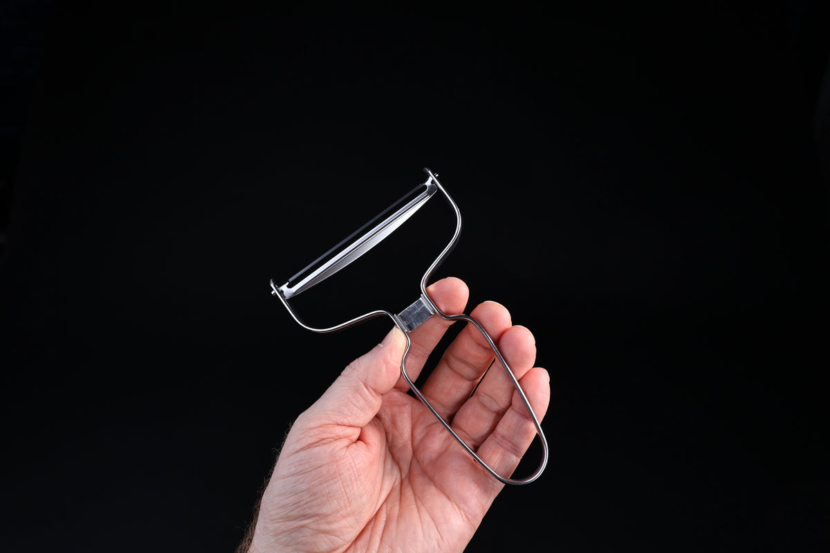 Japanese vegetable peeler large — held in hand, side view showing blade profile and loop handle construction