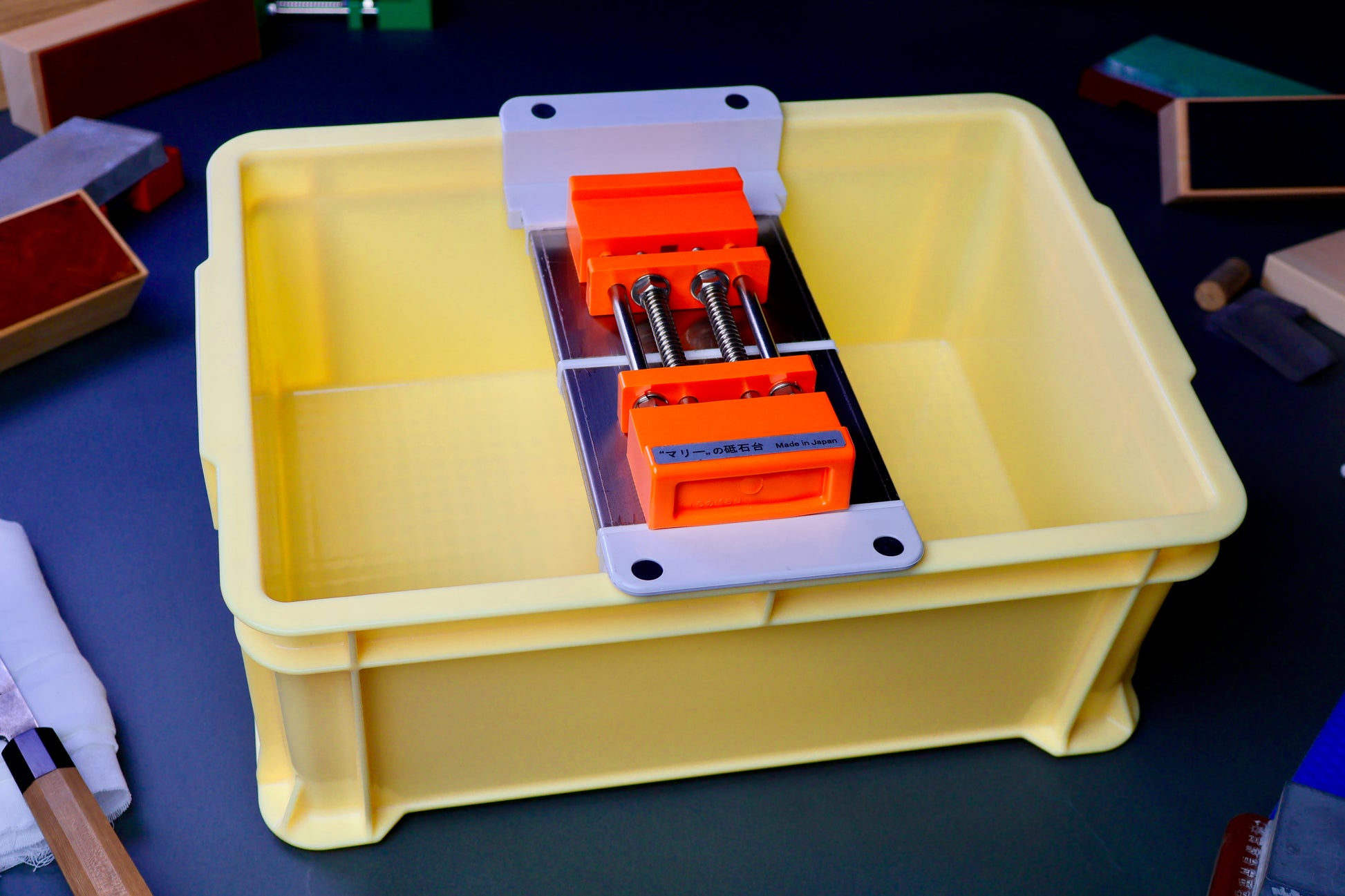 tall yellow box holding whetstone bridge and rubber holder orange color surrounded by knife sharpening accessories in dark background