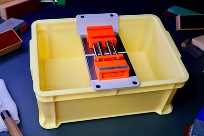 tall yellow box holding whetstone bridge and rubber holder orange color surrounded by knife sharpening accessories in dark background