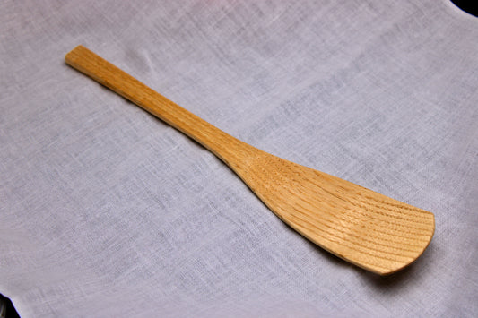 long smooth planed wooden spoon showing detailed wood grain pattern broad thin end for scoop contrasted on white cloth backdrop 