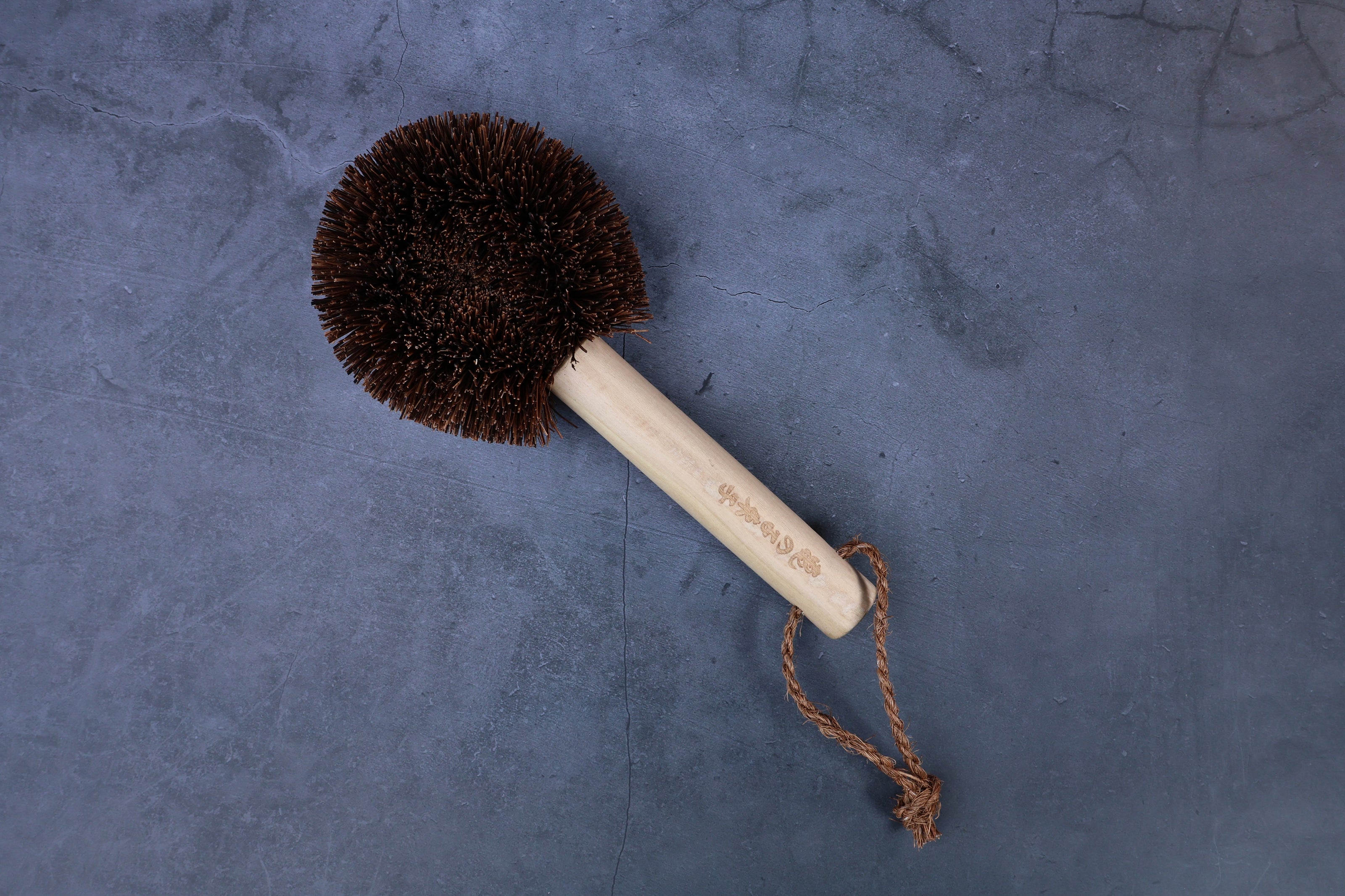 Kamenoko Ironware Pro Scrubber on concrete, showing engraved Japanese handle text and jute hanging loop clearly