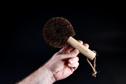 Kamenoko Ironware Pro Scrubber held in hand against black, showing full round bristle head from front