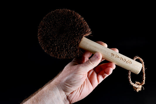 Kamenoko Ironware Pro Scrubber held in hand against black, showing handle engraving and bristle head from side