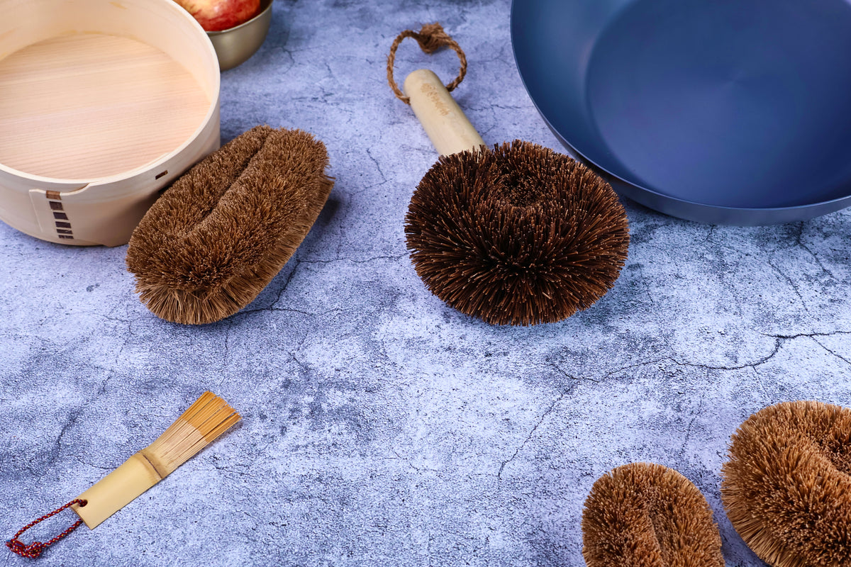 Kamenoko Ironware Pro Scrubber on concrete with bento box, carbon steel pan, and other kitchen tools, styled scene