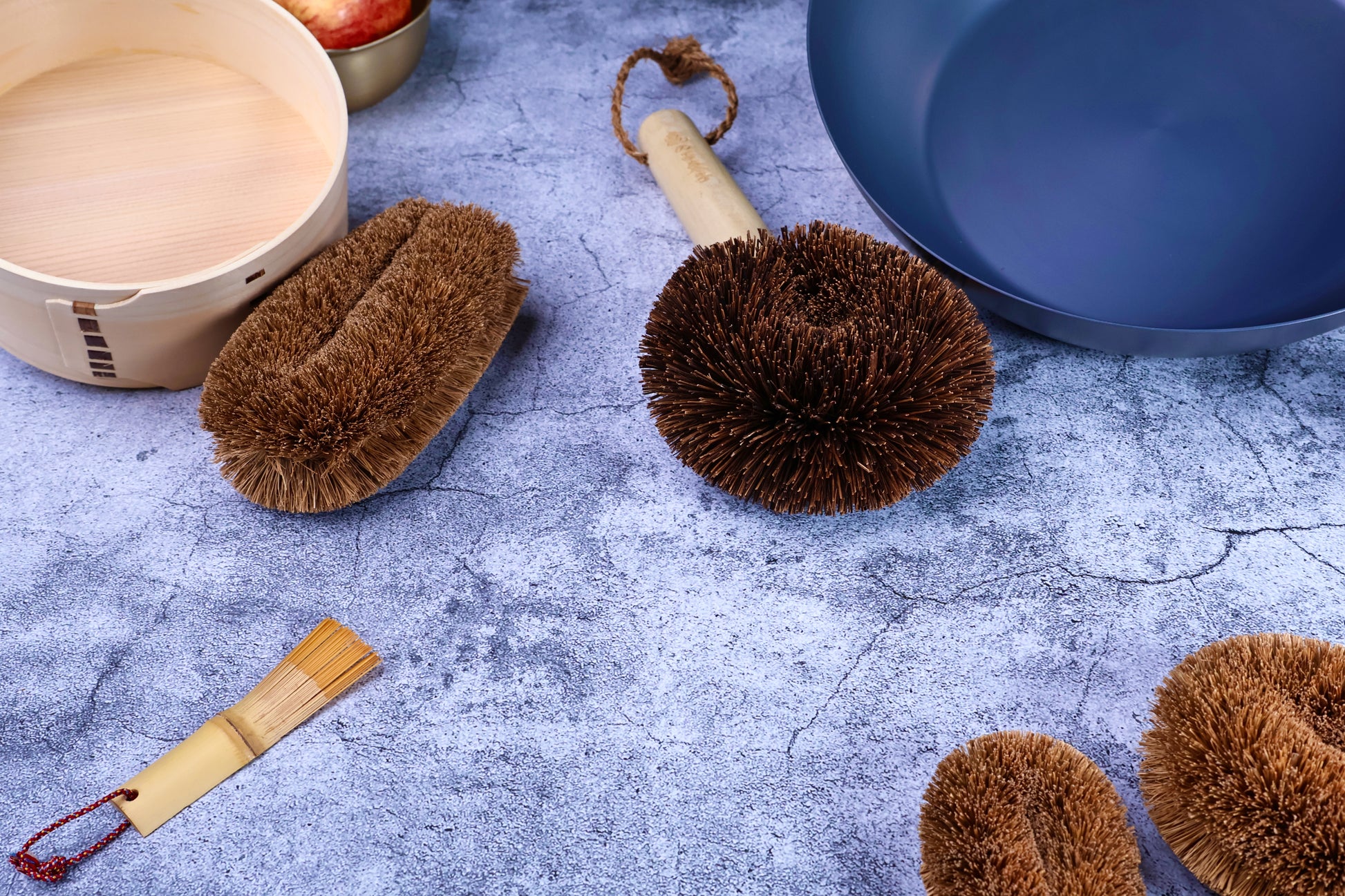Kamenoko Ironware Pro Scrubber on concrete with bento box, carbon steel pan, and other kitchen tools, styled scene