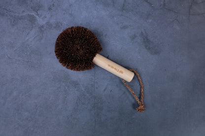 Single Kamenoko Ironware Pro Scrubber on concrete, showing round coconut fiber head and engraved wood handle