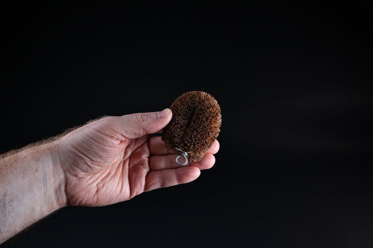 Kamenoko Tawashi palm-size scrub brush — held in open hand showing compact size and hanging loop