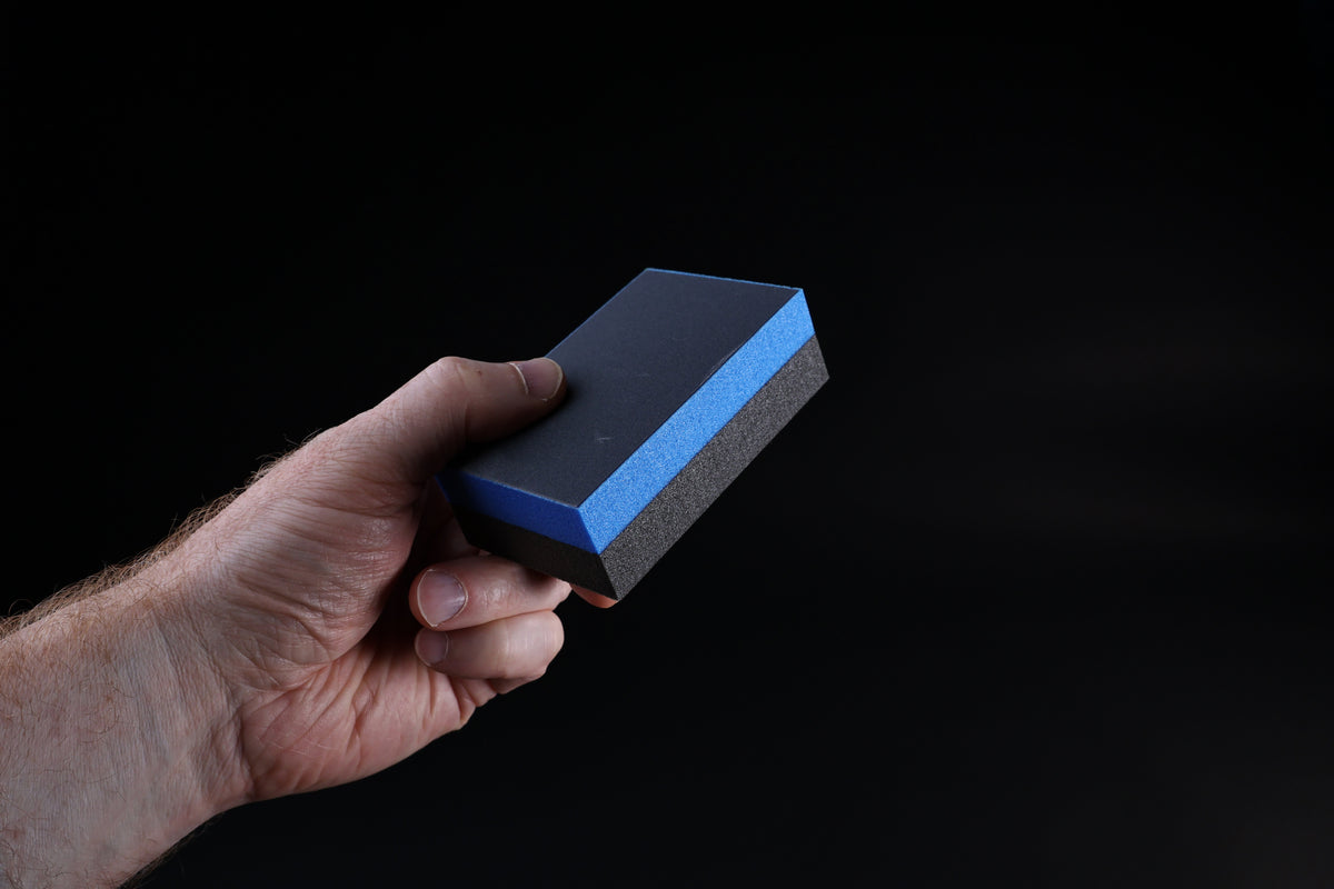 Kato Sangyo cutting board scraper — held in hand showing dual abrasive faces and blue foam core side profile