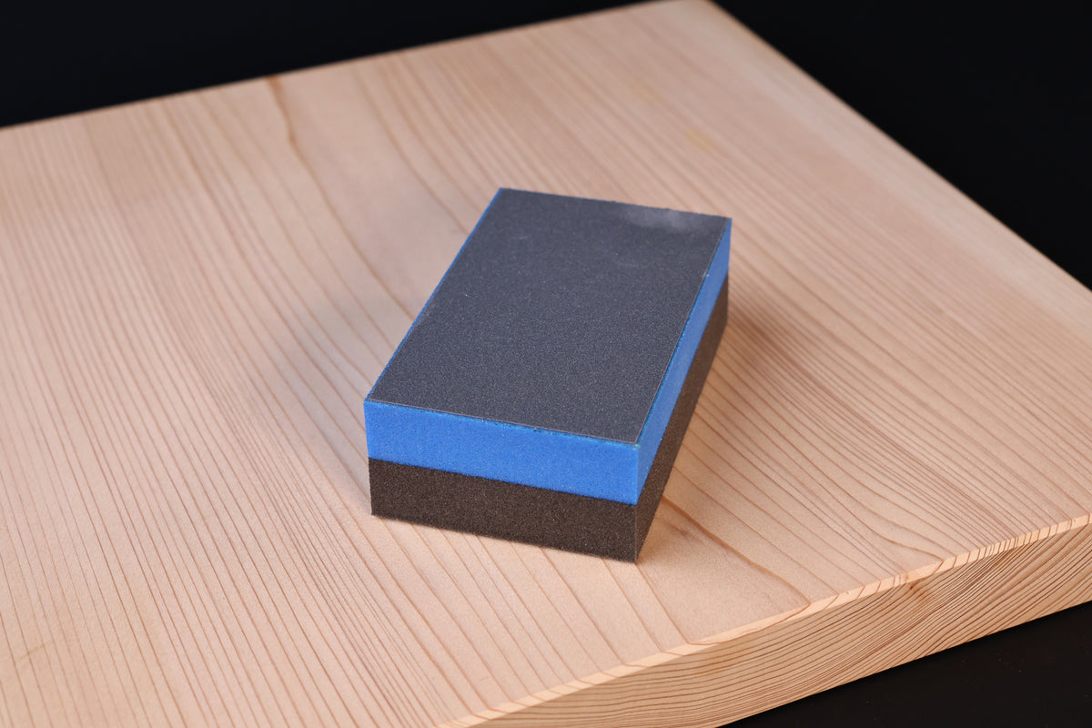 Kato Sangyo cutting board scraper — top view on hinoki board showing fine abrasive face and blue foam layer