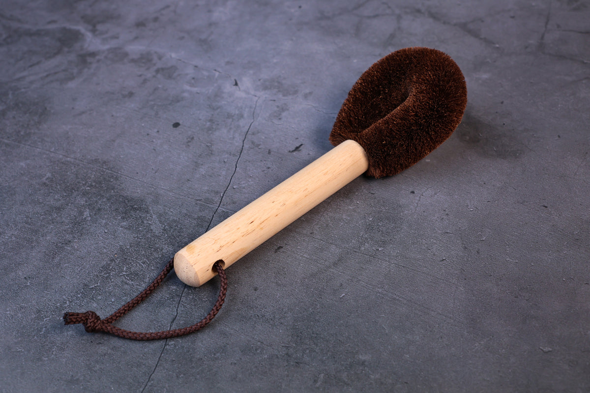 Kitayama Masatsumu tawashi brush resting on its side, showing the wooden handle, cord loop, and palm-fiber bristle head