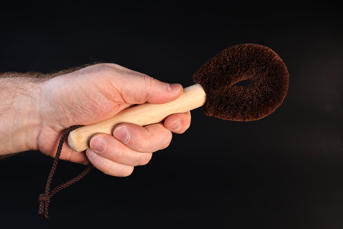 Kitayama Masatsumu palm-fiber tawashi brush held by the wooden handle, bristle head facing forward against a dark background