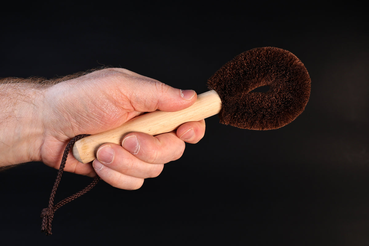 Kitayama Masatsumu palm-fiber tawashi brush held by the wooden handle, bristle head facing forward against a dark background