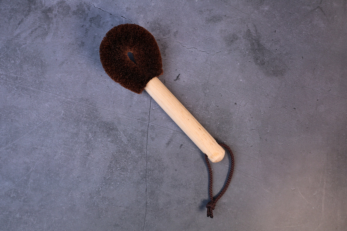 Kitayama Masatsumu tawashi brush with a round palm-fiber head and long wooden handle with hanging loop, seen from above