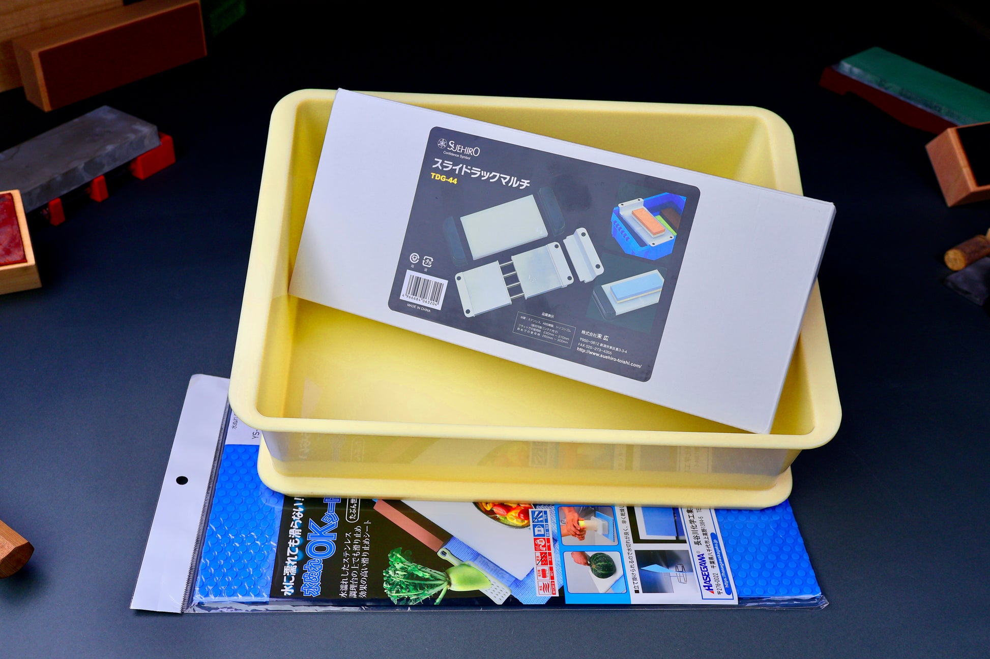 frontal shot of kitchen chef knife sharpening kit with suehiro multi rack hasegawa non slip mat and yellow open box with dark grey blue background 