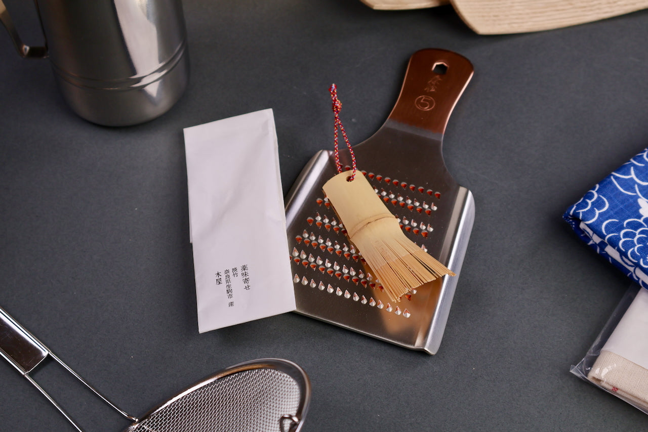 yakumiyosa bamboo scraper sitting on Oroshigane copper grater kiya brand paper beside surrounded by japanese kitchenware dark grey background