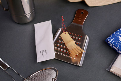 yakumiyosa bamboo scraper sitting on Oroshigane copper grater kiya brand paper beside surrounded by japanese kitchenware dark grey background