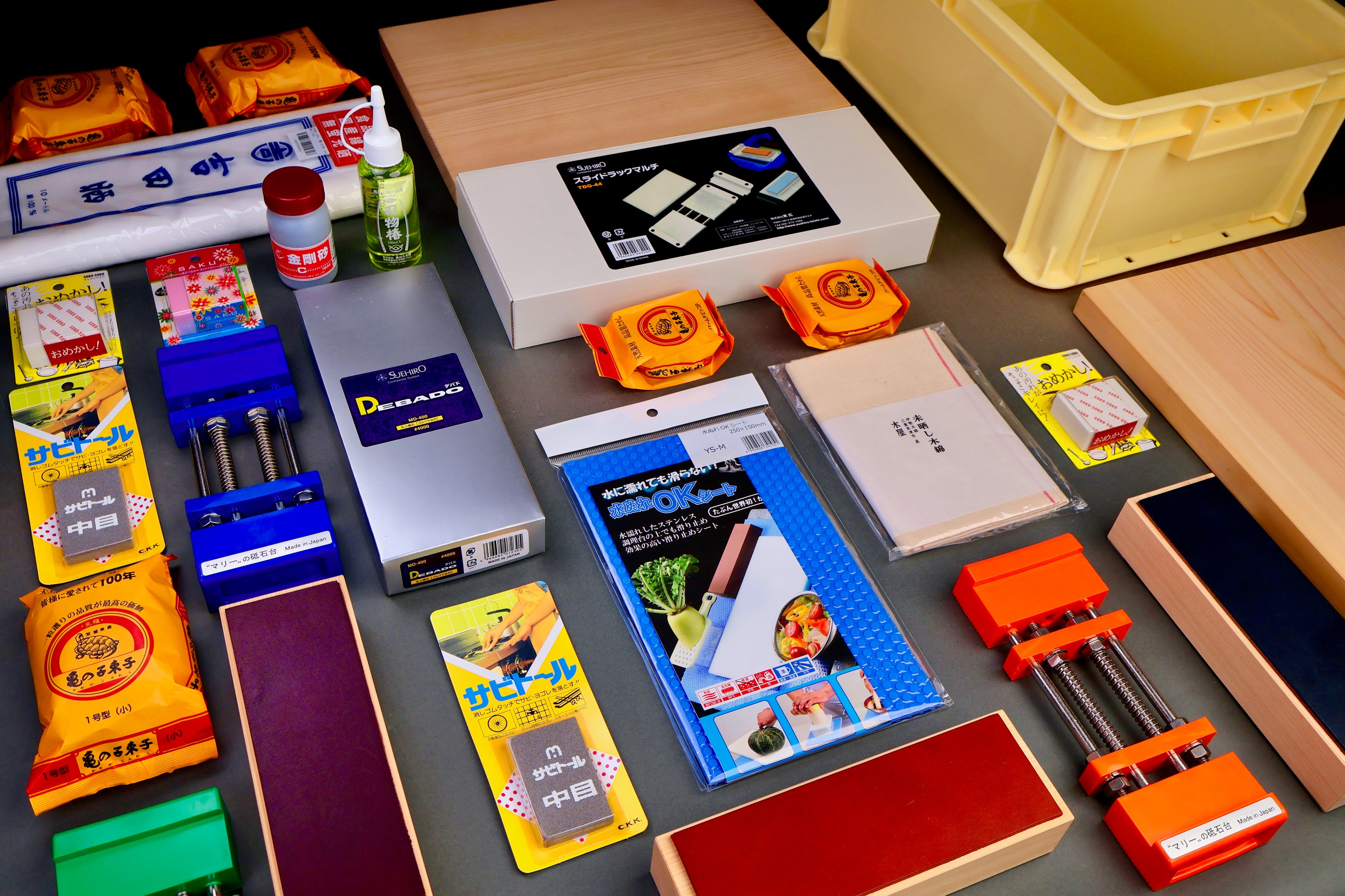 multiple knife sharpening products white towels blue whetstone holder rust eraser leather knife strop bright orange on grey backdrop