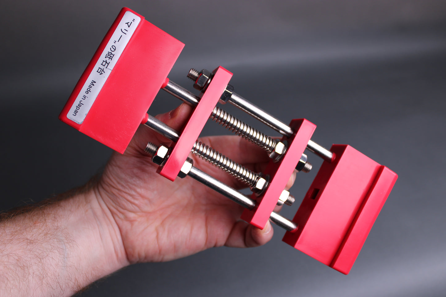 hand holding red whetstone holder rectangle shape springs rods dark background