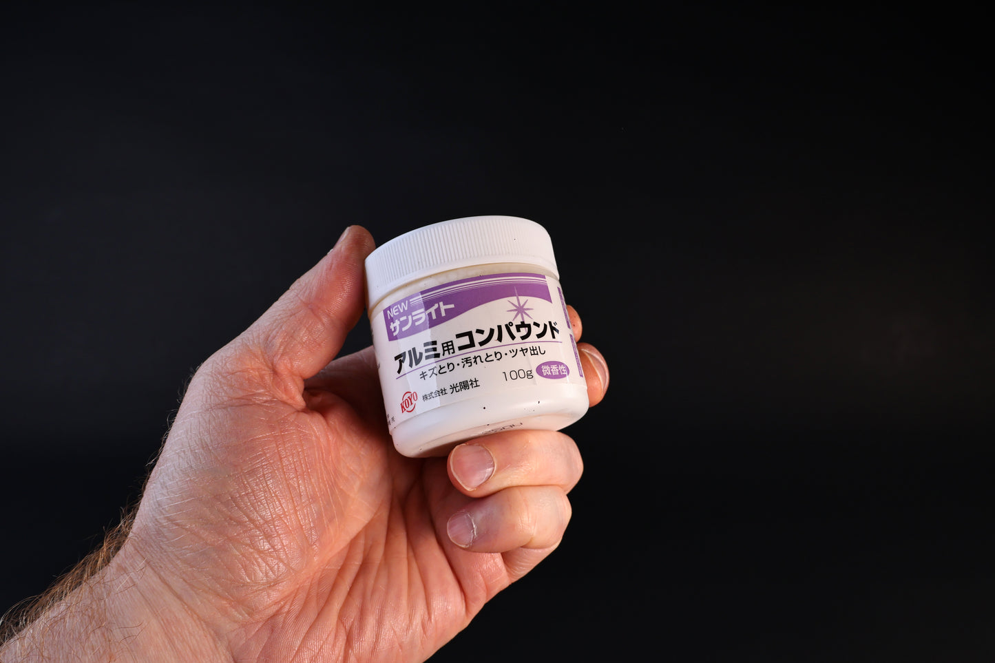 Koyo New Sunlite aluminum polishing compound in a 100g white jar with purple label, held against a dark background