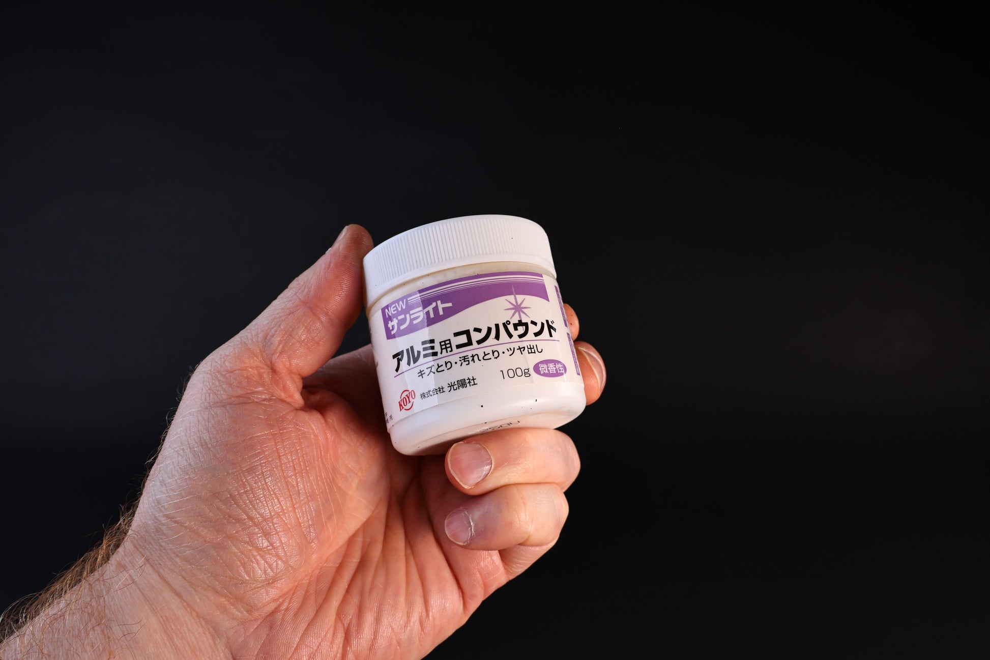 Koyo New Sunlite aluminum polishing compound in a 100g white jar with purple label, held against a dark background