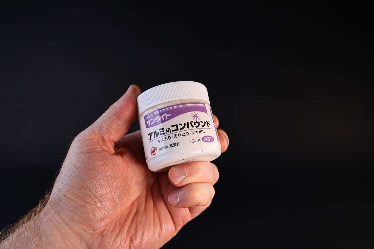 Koyo New Sunlite aluminum polishing compound in a 100g white jar with purple label, held against a dark background