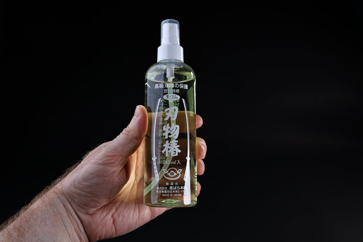 Kurobara tsubaki camellia oil 245ml spray bottle held in hand showing size and Japanese label on black background