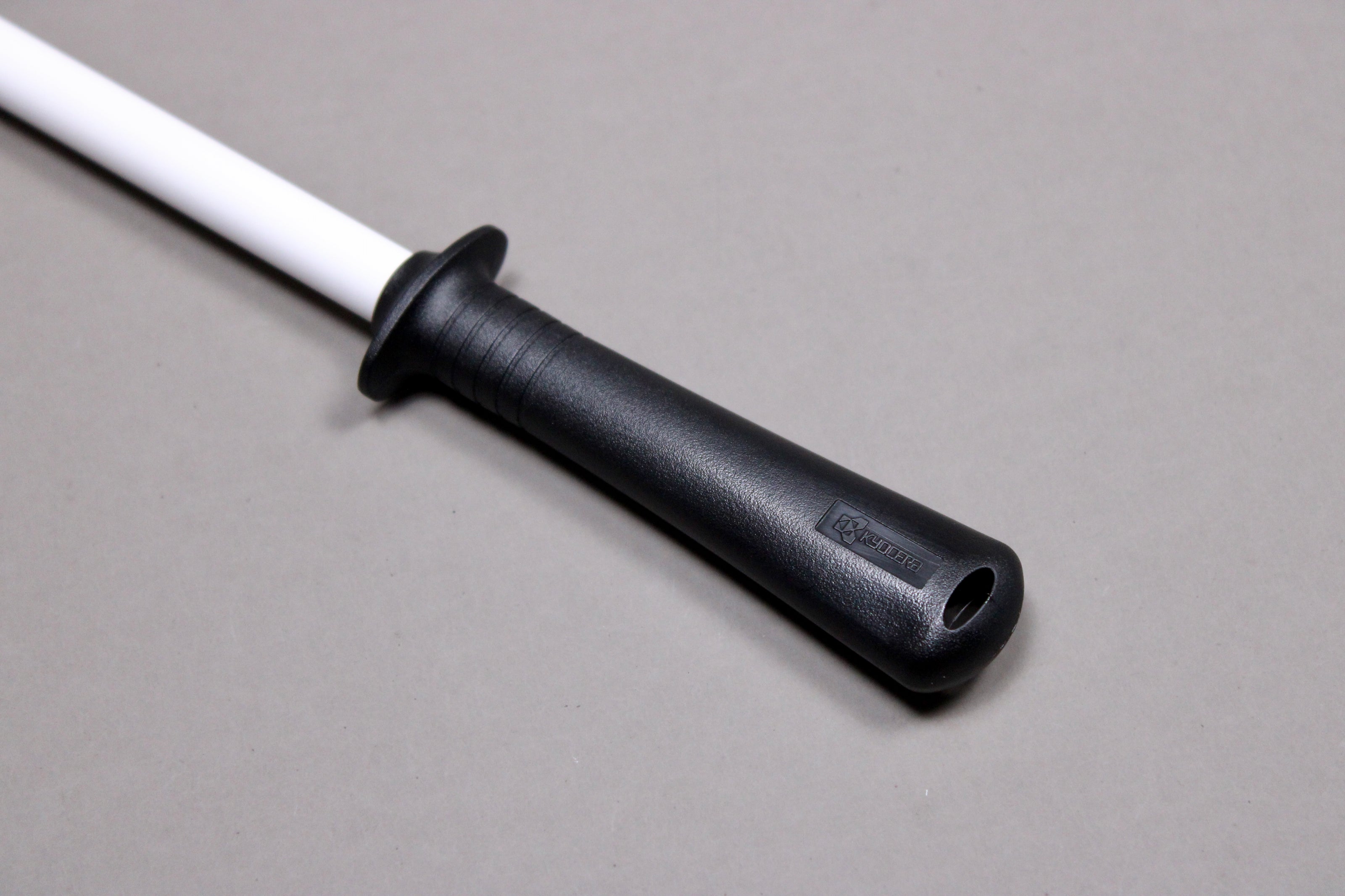 close up of plastic black handle on white ceramic honing rod angled on grey background