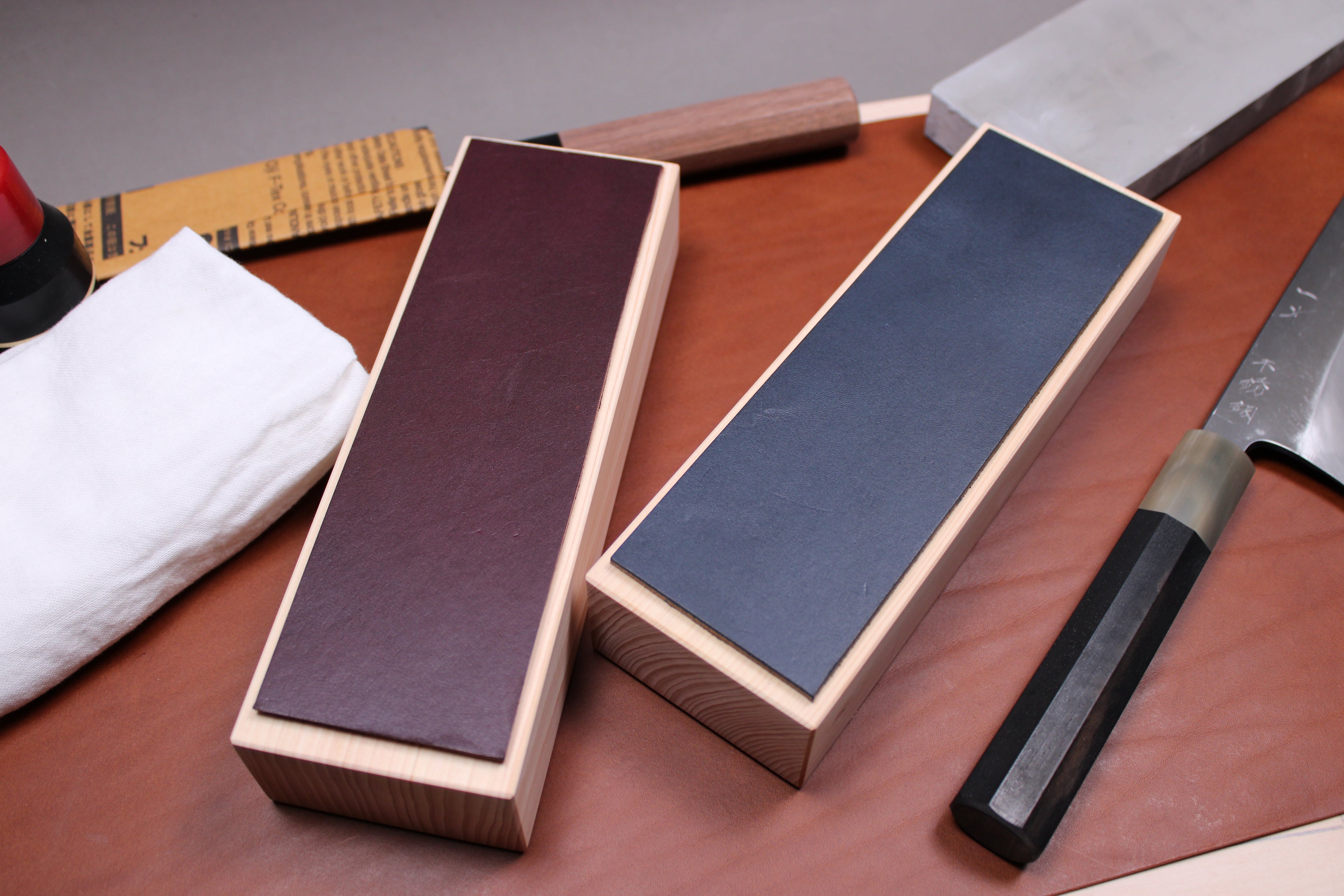 hinoki leather knife strops plum and midnight showcasing exceptional draw and feel surrounded by sharpening supplies by morihei hitohira yoshida sarashi sakai kikumori with workshop background
