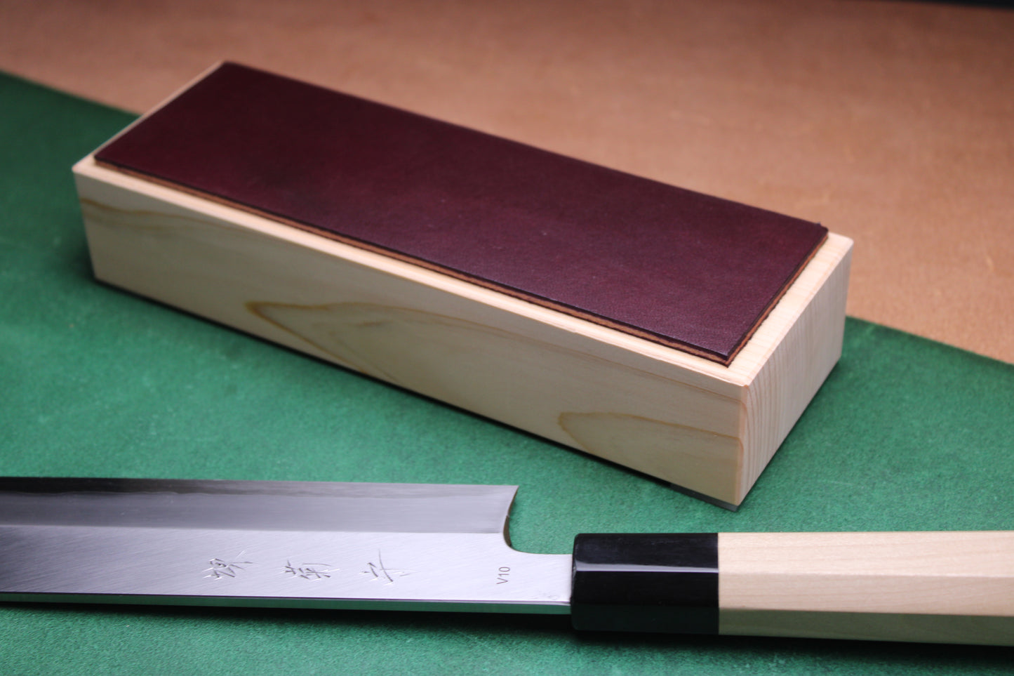 knife strop made of English bridle leather colored plum purple attached to sturdy tall smooth hinoki wood base sakai kikumori japanese usuba vegetable knife foreground with background faded green and brown