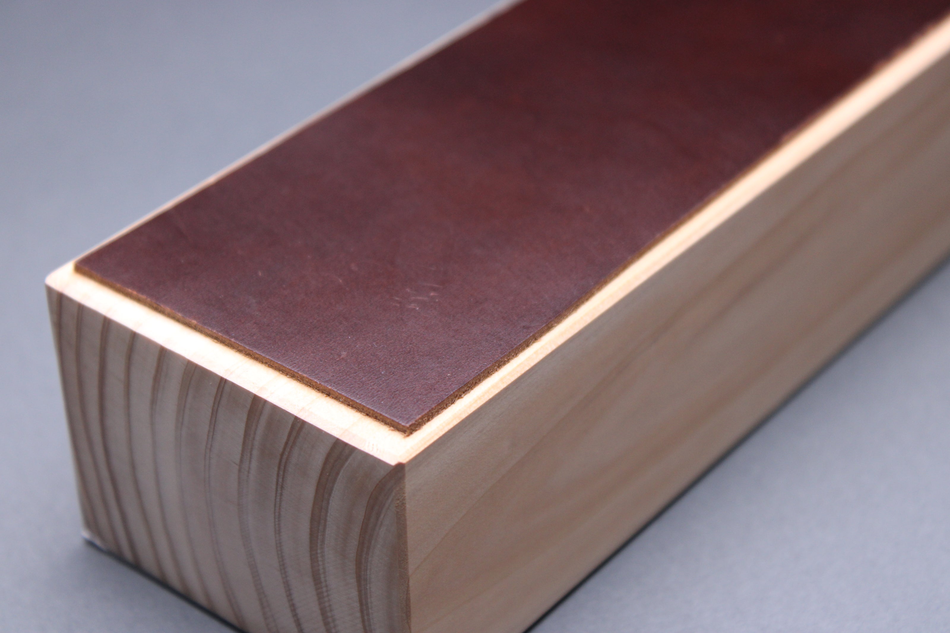 textured surface of pecan deep brown leather perfect for knife stropping atop sturdy tall hinoki wood base adequate height for knuckle clearance with grey background closeup shot