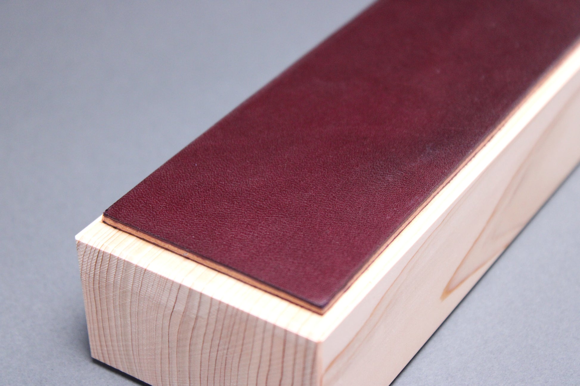 textured surface of plum purple leather perfect for knife stropping atop sturdy tall hinoki wood base adequate height for knuckle clearance with grey background closeup shot