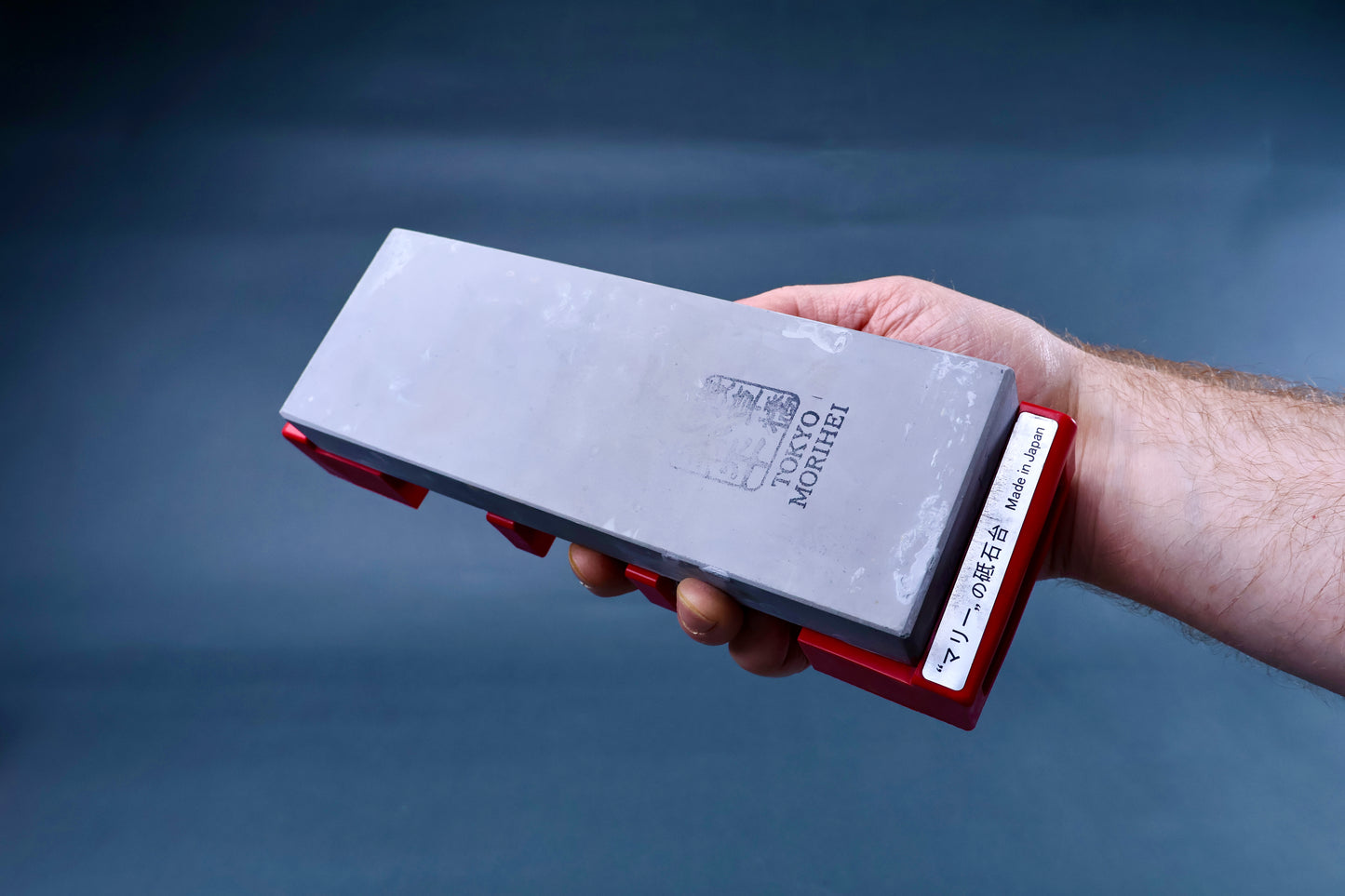 Marie's stone holder red held in hand with Tokyo Morihei whetstone loaded, showing Made in Japan label on blue-grey background