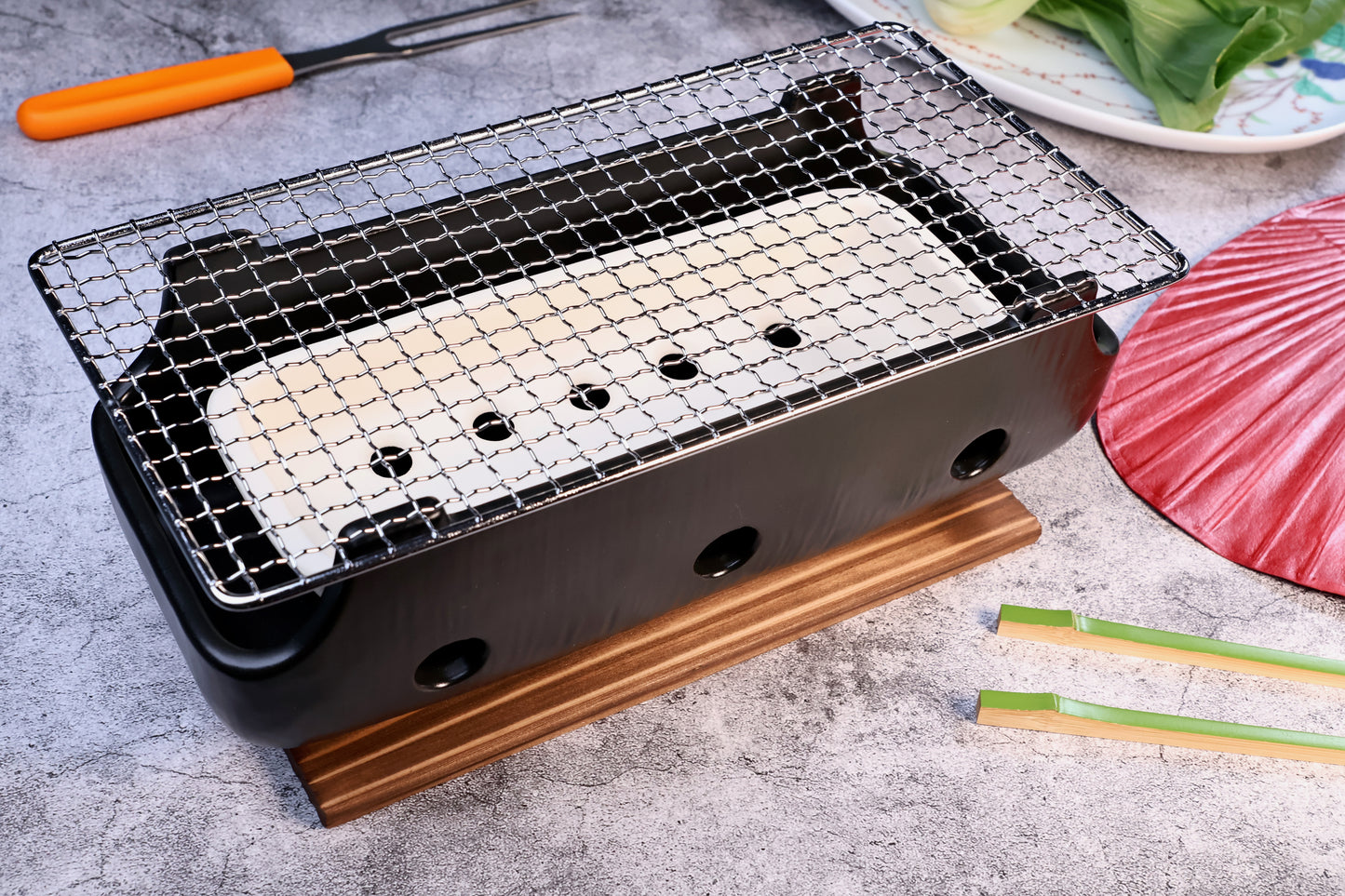 Misuzu Pottery Banko Yaki Konro Grill, lifestyle shot on concrete with Japanese fan, chopsticks, and leafy greens