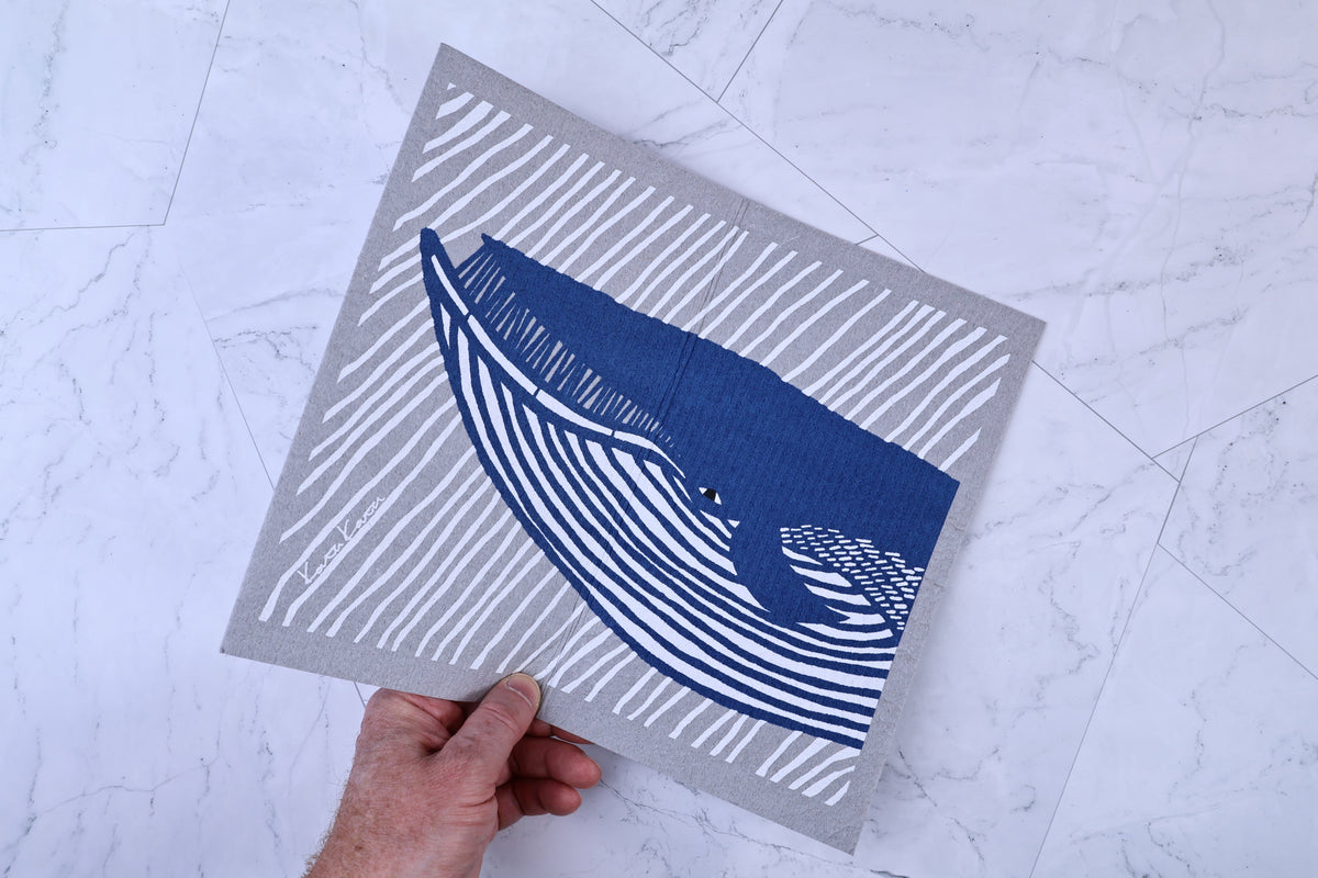 Morikatsu Katakata whale towel held at angle on marble, showing whale print and artist signature in corner