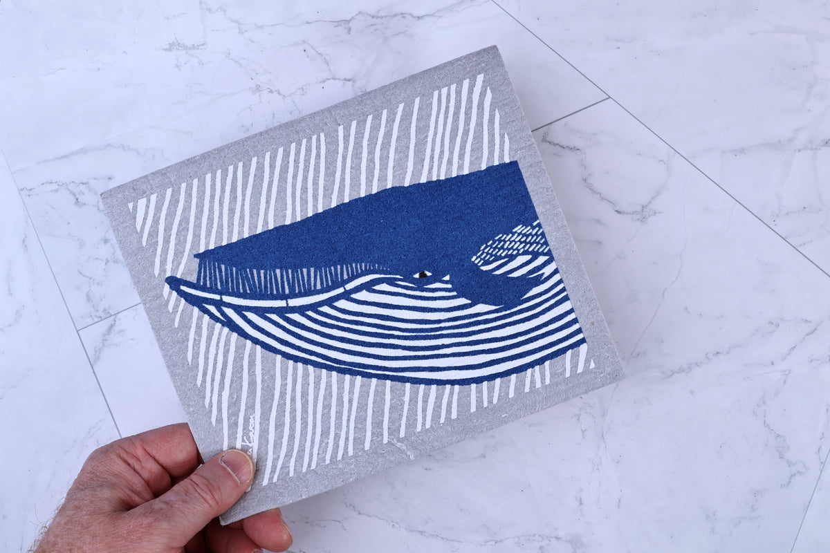 Morikatsu Katakata whale towel held in hand on white hex tile, full blue whale design on gray ground visible