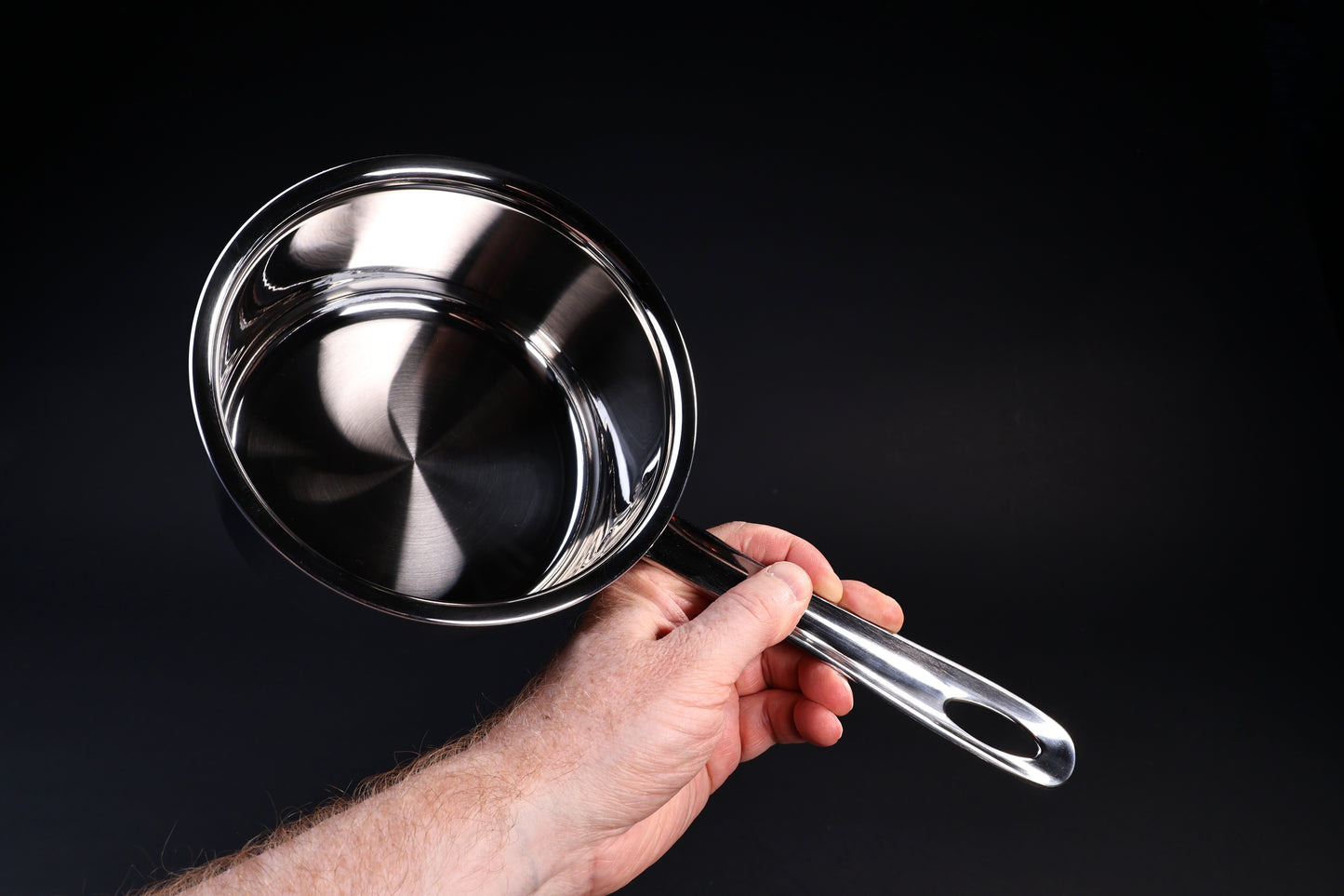 Mt. Fuji Steel Clad saucepan 16cm held in hand showing interior, straight walls, and size on black background
